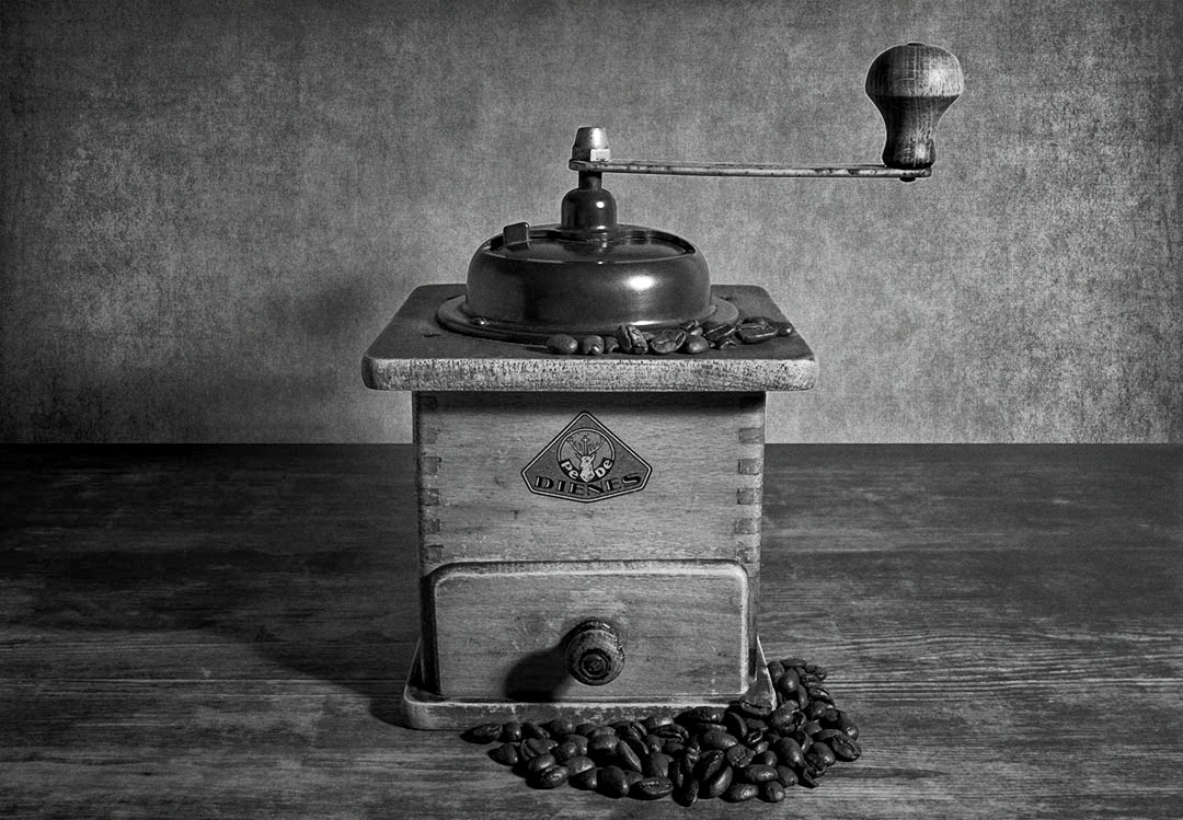 Eine alte Kaffeemühle, dekoriert mit einigen Kaffeebohnen, auf einem alten Tisch